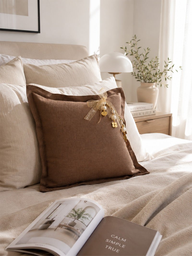 Coussin MIYA MARRAKECH No.50 en lin moka glacé avec perles nacrées dans une chambre contemporaine lumineuse.
