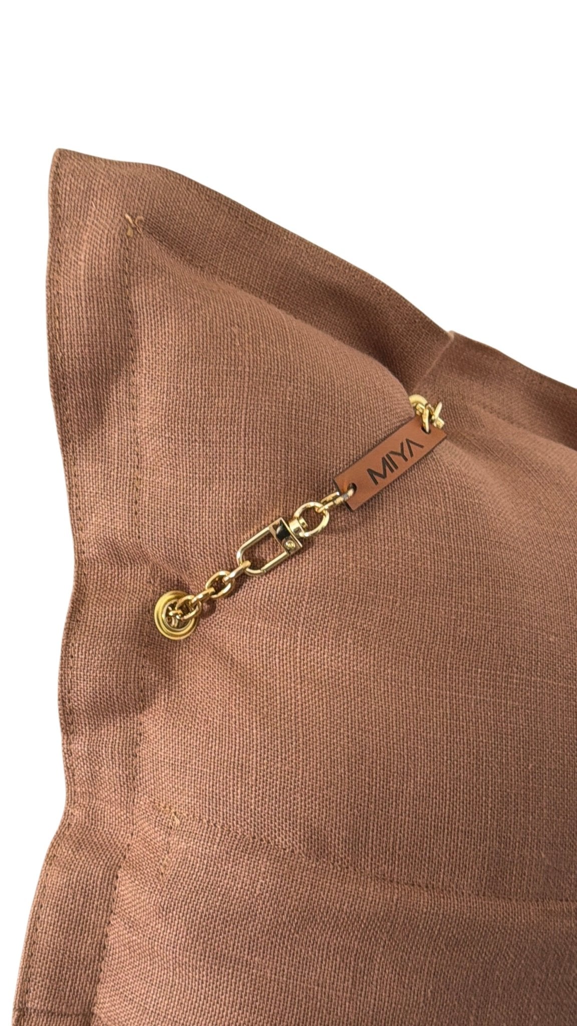 Détail du coussin artisanal MIYA en lin lourd moka glacé mettant en valeur la texture du tissu, la chaîne dorée et l’étiquette signature MIYA.