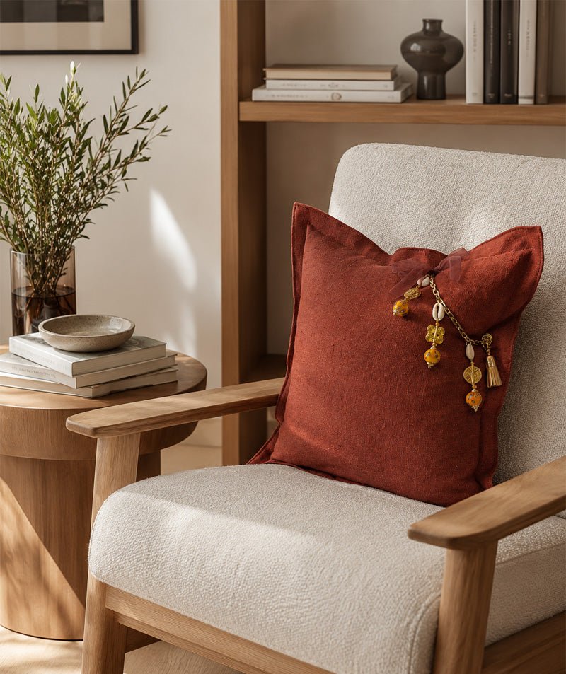 Terracotta heavy linen cushion with signature tassel in a modern contemporary interior with oak wood furniture and cream bouclé armchair.