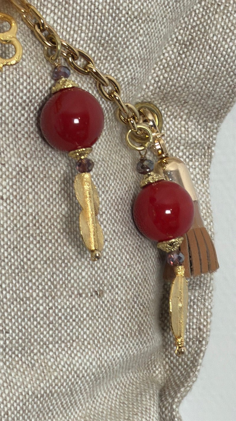 Détail de la pampille ZANZIBAR No.58 avec perles rouges et breloques dorées sur coussin en lin beige