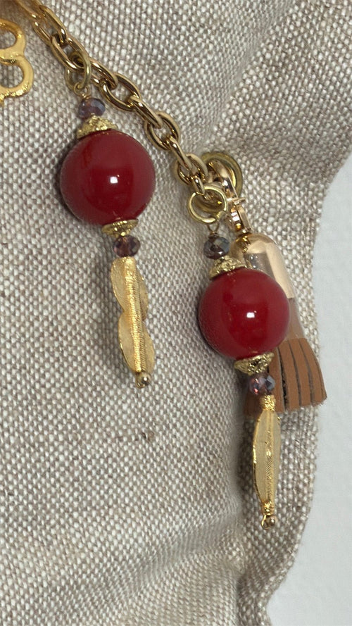 Détail de la pampille ZANZIBAR No.58 avec perles rouges et breloques dorées sur coussin en lin beige
