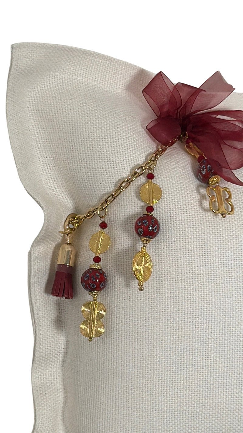 Détail artisanal MIYA avec ruban bordeaux, perles rouges et finitions dorées inspirées des poids Ashanti.