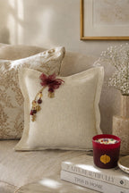 Coussin artisanal MIYA en lin blanc mis en scène dans un intérieur contemporain avec bougie bordeaux et matières naturelles.