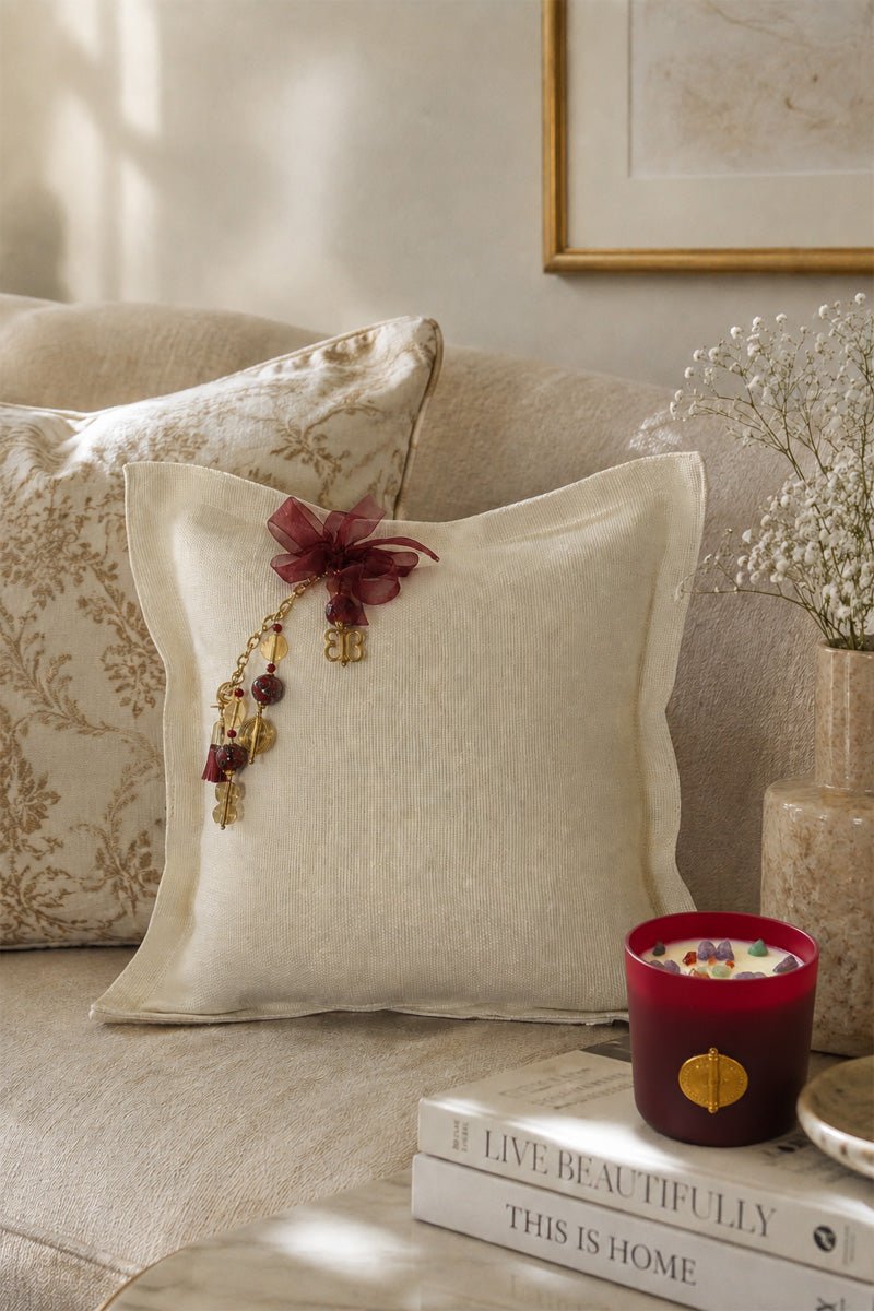 Coussin artisanal MIYA en lin blanc mis en scène dans un intérieur contemporain avec bougie bordeaux et matières naturelles.