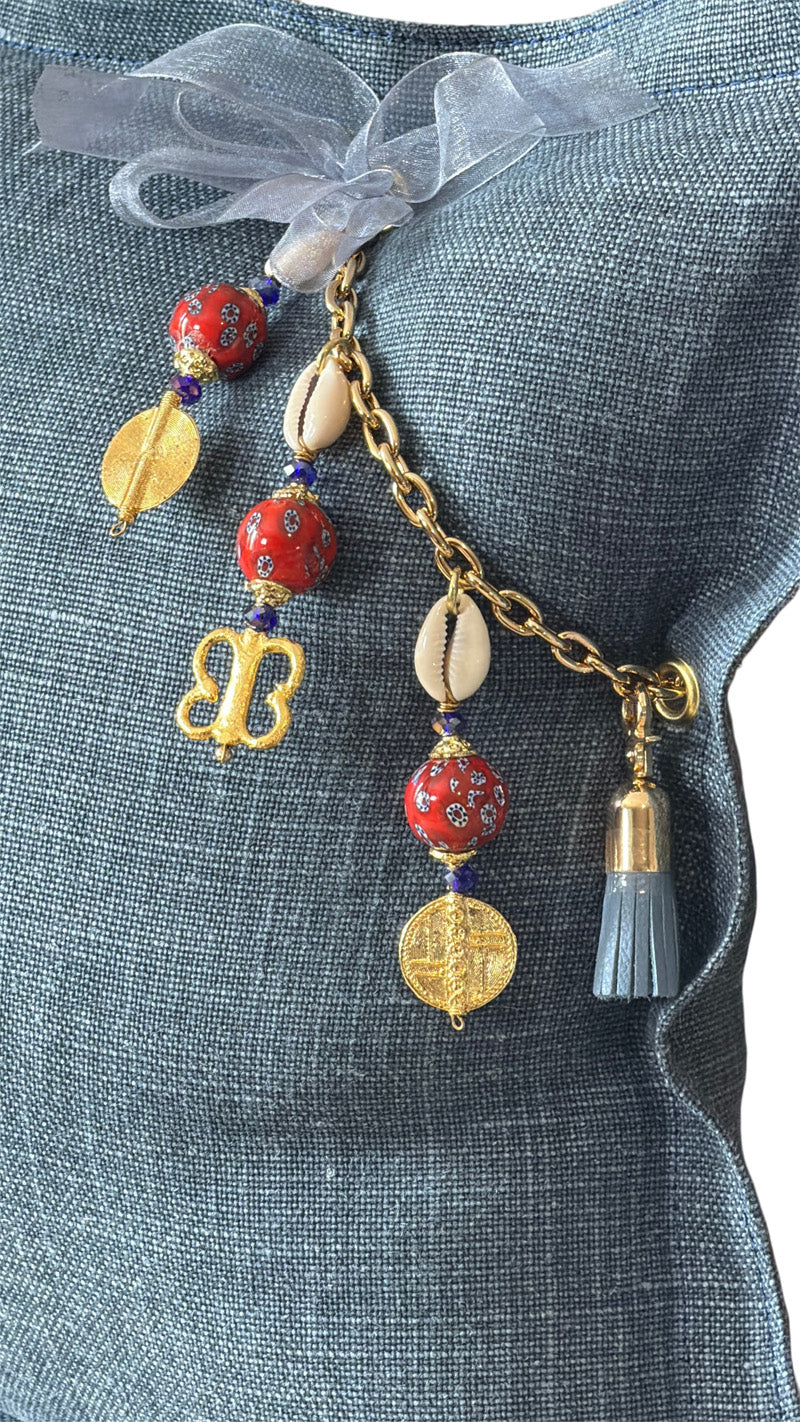 Close-up of the MIYA signature tassel with African beads, cowries and Ashanti weights on heavy blue linen.