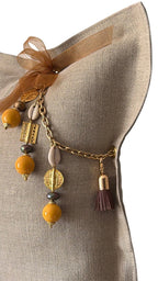 Pampille signature MIYA BALI No.98 avec perles africaines jaunes, cauris et poids Ashanti sur coussin en lin grège.