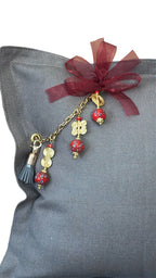 Close-up of MIYA's signature tassel with red African beads and Ashanti weights on grey heavy linen.