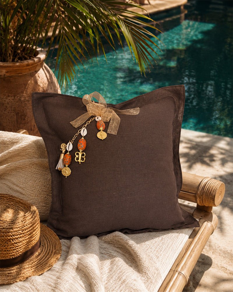 Coussin en lin lourd marron MIYA avec pampille signature au bord d’une piscine dans une ambiance bohème chic inspirée du voyage.