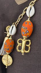 Détail pampille signature MIYA avec perles artisanales orange, cauris et poids Ashanti dorés.