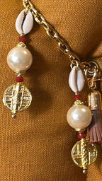 Pampille signature Marrakech No.51 avec cauris, perles nacrées et détails dorés inspirés des poids Ashanti sur coussin en lin moutarde MIYA.