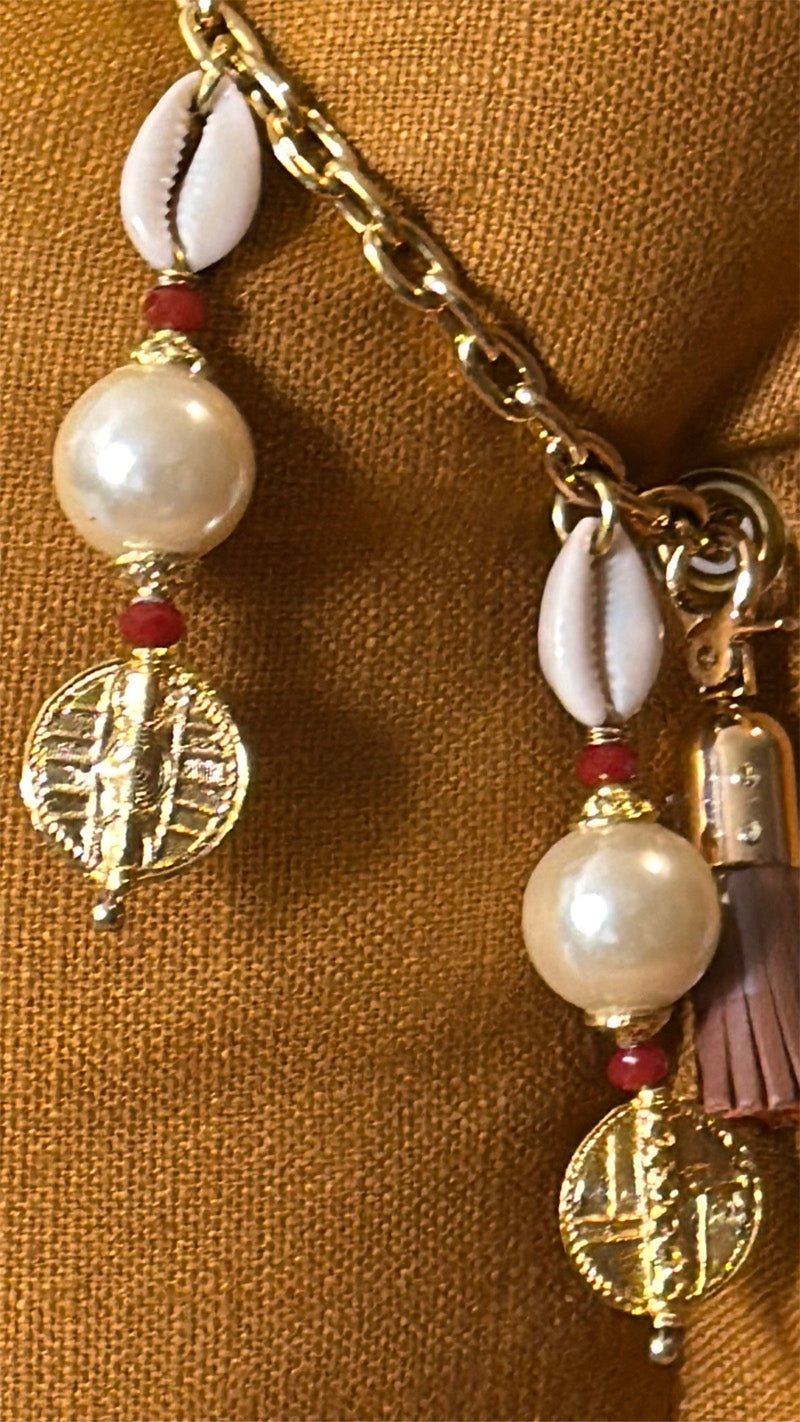 Pampille signature Marrakech No.51 avec cauris, perles nacrées et détails dorés inspirés des poids Ashanti sur coussin en lin moutarde MIYA.