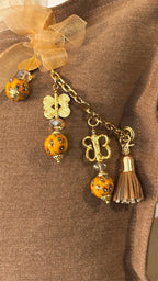 Pampille signature MIYA MARRAKECH No.97 avec perles africaines jaunes, poids Ashanti et pompon sur coussin en lin caramel.