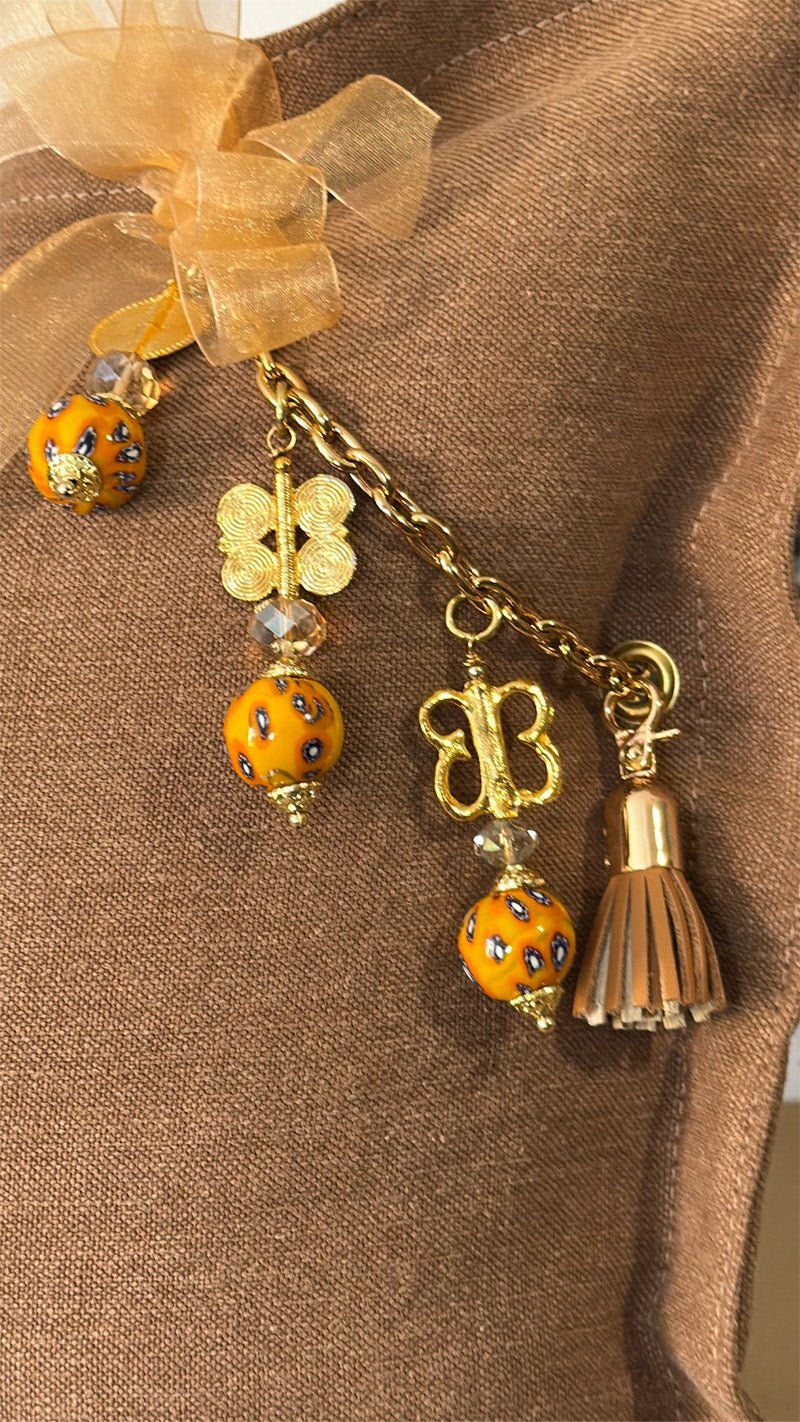 Pampille signature MIYA MARRAKECH No.97 avec perles africaines jaunes, poids Ashanti et pompon sur coussin en lin caramel.