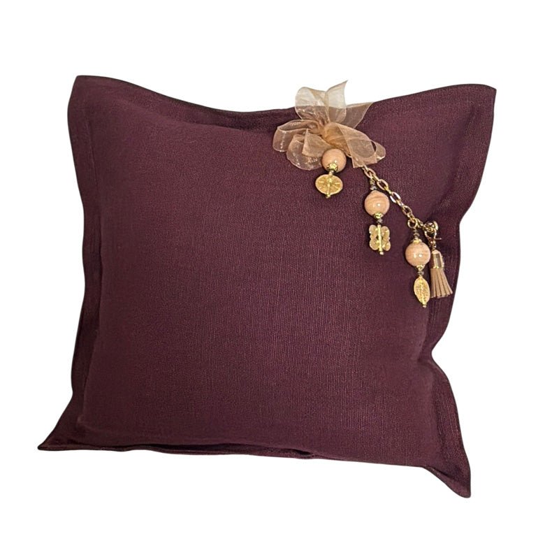 Coussin artisanal prune MIYA en lin avec pampille signature, perles beige rosé, détails dorés et ruban champagne.