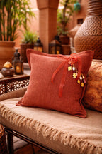 Coussin rose sienne avec pampille signature MIYA, ornée de poids Ashanti et perles, dans un décor inspiré de Marrakech.