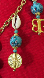 Pampille MIYA avec perles bleu turquoise, cauris et poids Ashanti sur coussin rouge