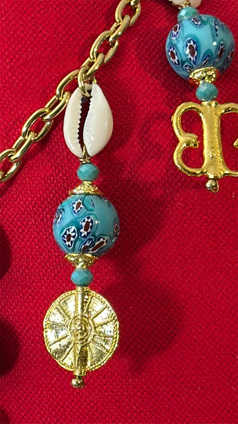 Pampille MIYA avec perles bleu turquoise, cauris et poids Ashanti sur coussin rouge