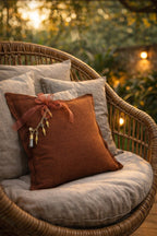 Coussin marron rouille avec pampille signature MIYA ornée de poids Ashanti et perles sur fauteuil en rotin