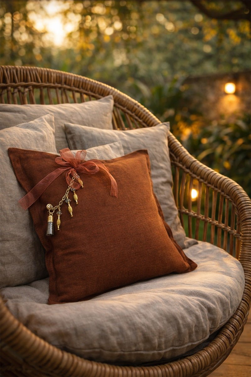 Coussin marron rouille avec pampille signature MIYA ornée de poids Ashanti et perles sur fauteuil en rotin