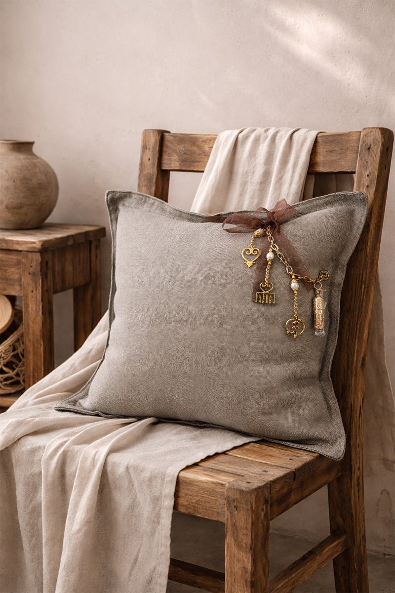 Coussin en lin taupe MIYA avec pampilles dorées et ruban brun rosé, posé sur une chaise en bois dans un esprit Marrakech