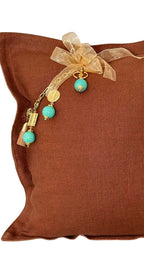 Coussin en lin lourd terracotta MIYA avec pampille signature, perles vert d’eau et détails dorés.