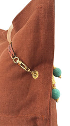 Vue profil du coussin en lin lourd terracotta MIYA avec pampille signature et perles vert d’eau.