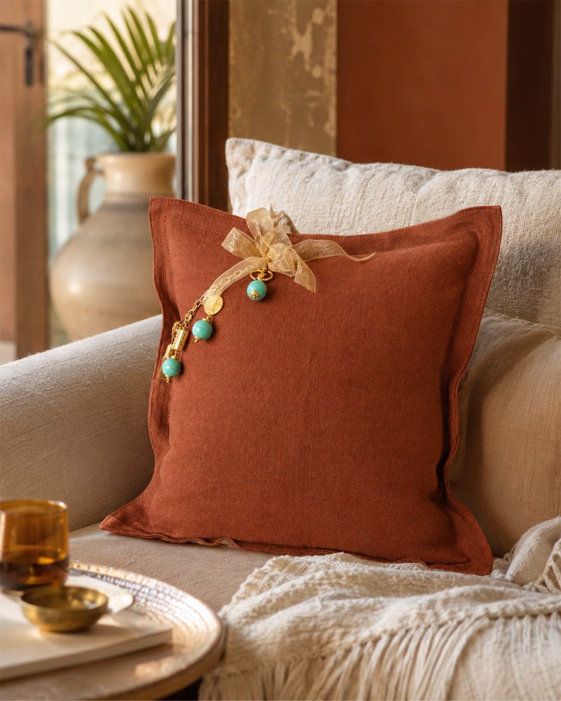 Coussin en lin lourd terracotta MIYA avec pampille signature et perles vert d’eau dans un intérieur bohème chic inspiré des voyages.