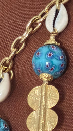 Zoom sur le coussin artisanal MIYA mettant en valeur la texture du tissu, les perles turquoise artisanales, les cauris et les finitions de la pampille MARRAKECH No.49.