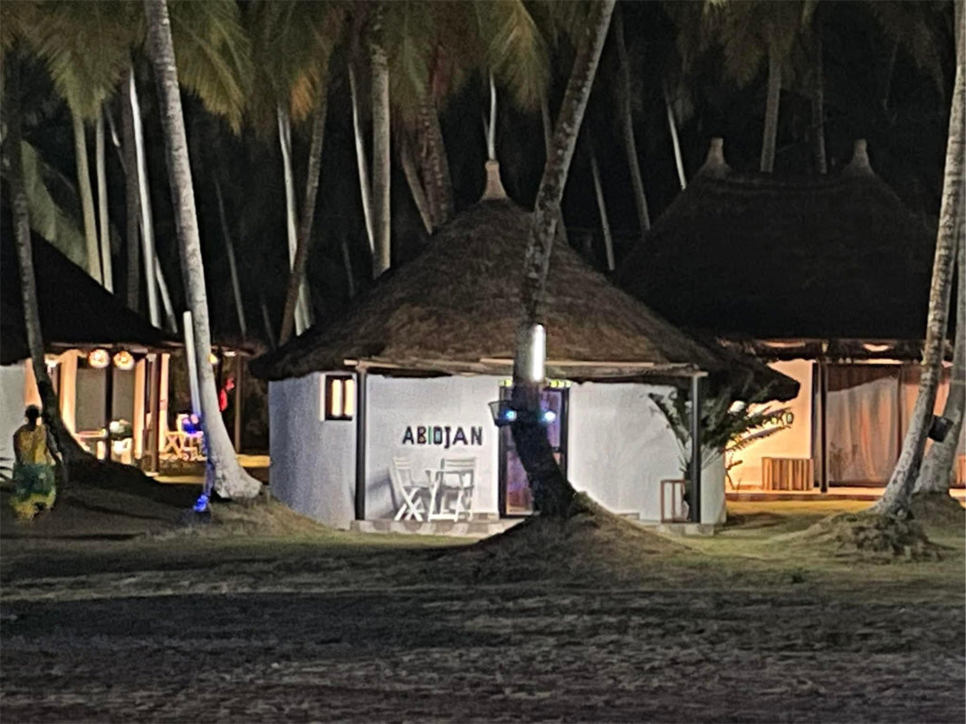Hutte ronde au toit de chaume éclairée la nuit sous les palmiers sur une plage tropicale.