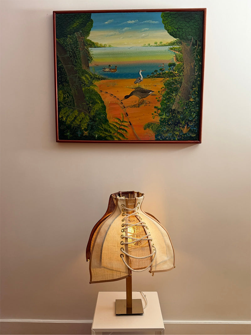 Lampe corsetée posée sur un socle marbre sous un tableau