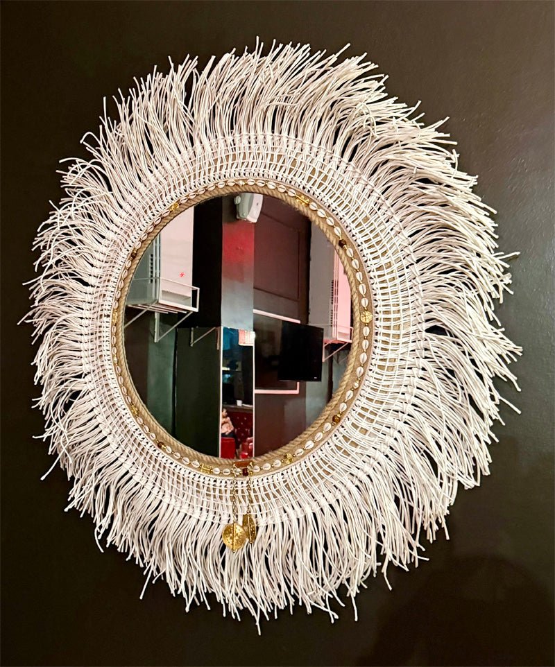Miroir décoratif en fibres tressées avec effet soleil, franges naturelles et finitions dorées, vu en angle – MIYA